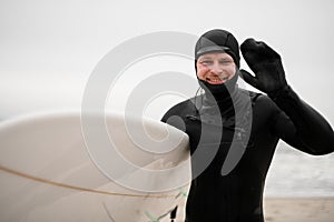 Happy smiling male surfer standing on seashore in wet clothes, water drops on face
