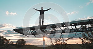 Happy smiling man with a beard is standing on the wing of an abandoned small plane with his arms spread and raised