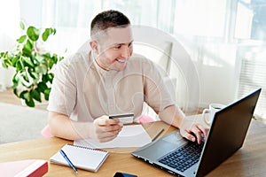 Happy smiling man booking hotel on laptop with credit card at home office, copy space. Technology, banking, paying, online.