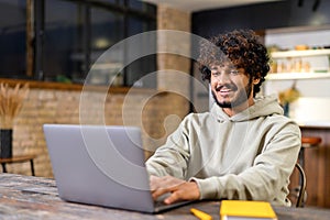 Happy smiling man distantly working from home. Successful male freelancer sitting at the desk, using laptop, develop a