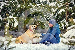 A happy smiling man and a dog sitting in a winter forest