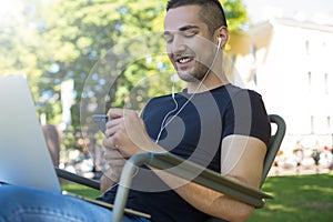 Happy smiling man freelance content writer listening to music via headphones and chatting on mobile phone