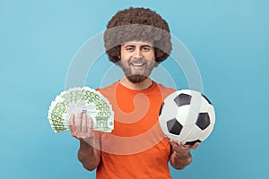 Happy smiling man holding soccer ball and fan of euro bills, sports betting, big win.