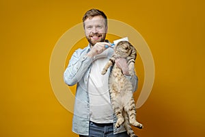 Happy, smiling man hugs his adorable, beautiful cat and jokingly cleans it with an adhesive tape roller.