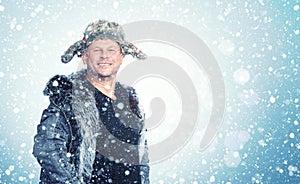 Happy smiling man in open winter clothes rejoices in falling snow