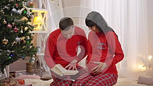 Happy smiling man reading book and kissing pregnant belly of smiling woman. Portrait of loving Caucasian husband and