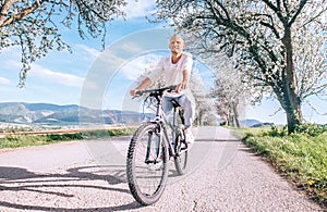 Happy smiling man riding a bicycle on the country road under blossom trees. Spring is comming concept image