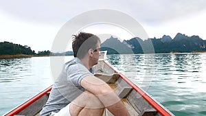 Happy Smiling Man Sitting on Wooden Boat and Sailing on Morning Blue Lake