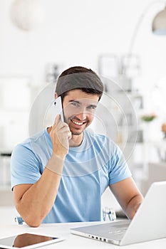 Happy smiling man talking over phone, working at laptop discusses ideas with the customer