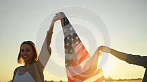 happy smiling man and woman, american family, walking in field at sunset with flag of USA with proud, celebration fourth