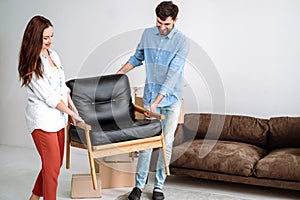 Happy smiling man and woman carry armchair in new home