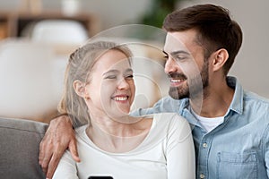 Happy smiling man and woman cuddle, using phone together