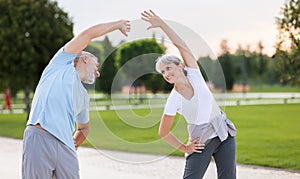 Happy smiling mature man and woman in sportswear stretching body while warming up together outdoors