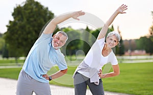 Happy smiling mature man and woman in sportswear stretching body while warming up together outdoors