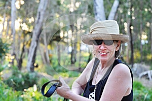 Happy smiling mature woman in hat on forest trail hiking