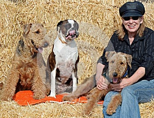 Happy smiling mature woman on hay bales cuddling pet dogs