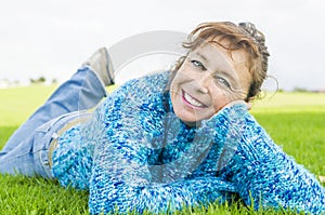 Happy smiling mature woman laying on grass