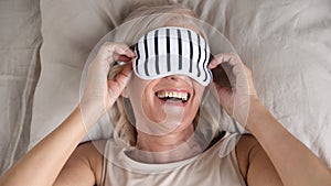 Happy smiling mature woman wearing sleeping mask lying in bed