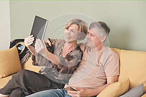 Happy smiling middle age couple with digital tablet computer having video call at home. online chat with family.