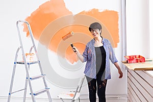 Happy smiling middle-aged woman painting interior wall of new house. Redecoration, renovation, apartment repair and