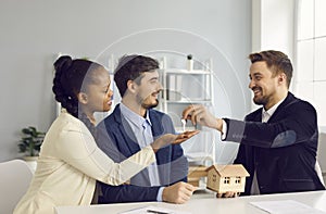 Happy smiling millennial multiethnic couple taking key from realtor agent