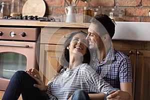 Happy smiling millennial spouses cuddling on kitchen floor celebrating moving
