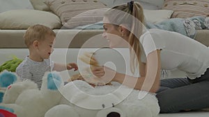 Happy and smiling mom with baby playing in living room at home with plush stuffed animals toys, sitting on the floor with pillows
