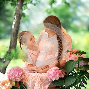 Happy smiling mom with a daughter child on a sunny summer day. Mother and girl kid in a beautiful blooming garden with gartensia