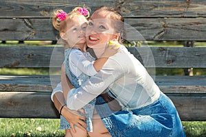 Happy smiling mom with a daughter child walking in garden and a dandelion flower is blowing merrily on a sunny summer