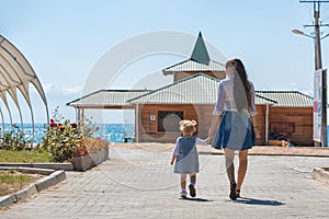 Happy smiling mom with a daughter child walking in garden and a dandelion flower is blowing merrily on a sunny summer