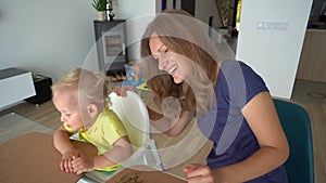 Happy smiling mom feeding her baby boy with cherry berry at home