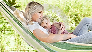 Happy and smiling mom hugs her little girl daughter child blue eyes with blond curly hair, together lying on the hammock in the