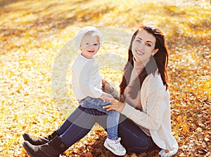 Happy smiling mom with little child playing in autumn park