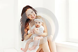 Happy smiling mother with baby at home in white room