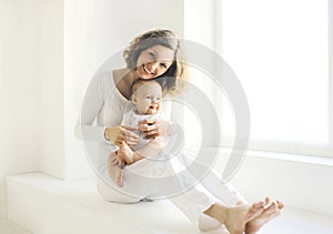 Happy smiling mother with baby home in white room near window