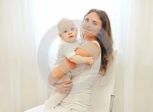 Happy smiling mother with baby sitting on chair at home