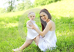 Happy smiling mother and baby sitting on the grass
