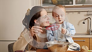 Happy smiling mother with baby son palying on kitchen while making bread dough. Concept of little chef, children cooking