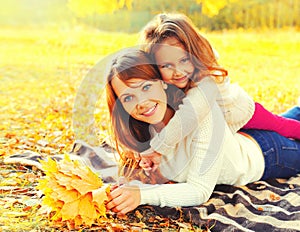 Happy smiling mother and child little girl with yellow maple leaves in sunny autumn park