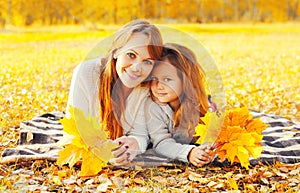 Happy smiling mother and child little girl with yellow maple leaves in sunny autumn park