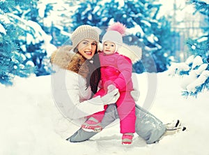Happy smiling mother and child sitting on snow in winter