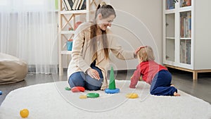 Happy smiling mother and cute baby boy crawling on soft carpet in living room