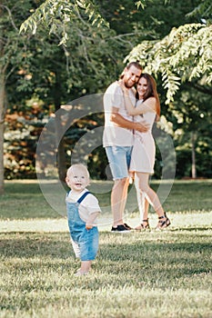 Happy smiling mother and father with baby boy in park outdoors. Family Caucasian mom and dad with son walking hugging in park on
