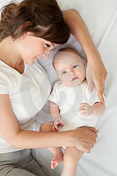 Happy smiling mother and her baby lying on bed at home, top view