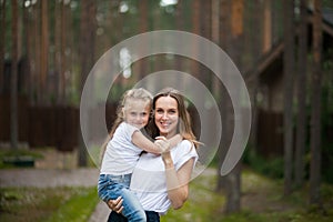 Happy smiling mother and her cute emotional little daughter child in white shirts and denim jeans are hugging and having fun