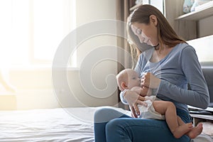 Happy smiling mother holding and breastfeeding her baby child at home