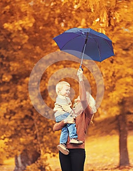 Happy smiling mother holding child with umbrella having fun together on autumn trees background