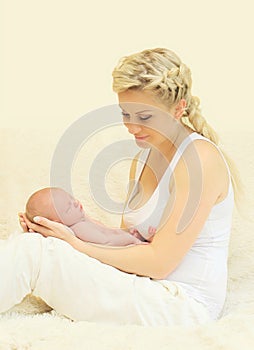 Happy smiling mother holding on hands sleeping infant home