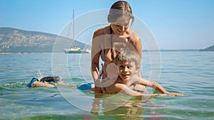 Happy smiling mother holding her little son learning swimming in sea at the beach. Family holiday, vacation and fun