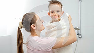 Happy smiling mother hugging and covering her son in bath towel after taking shower. Concept of hygine, children